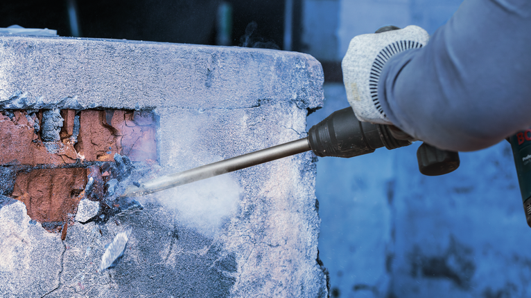 配戴安全設備的人員使用電動工具打破牆上的混凝土。.