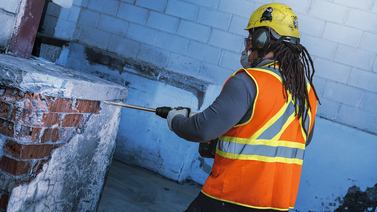 一名配戴安全設備的工人使用拆除工具拆除混凝土牆。.