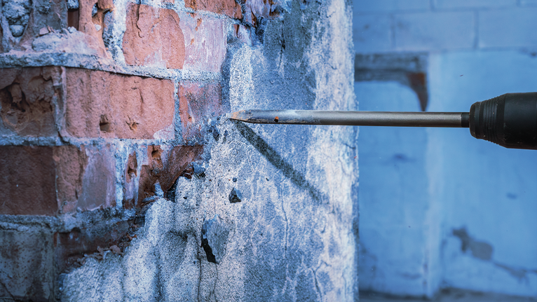 鑿子鑽頭將磚牆上的混凝土鑿破，產生灰塵和碎片。.