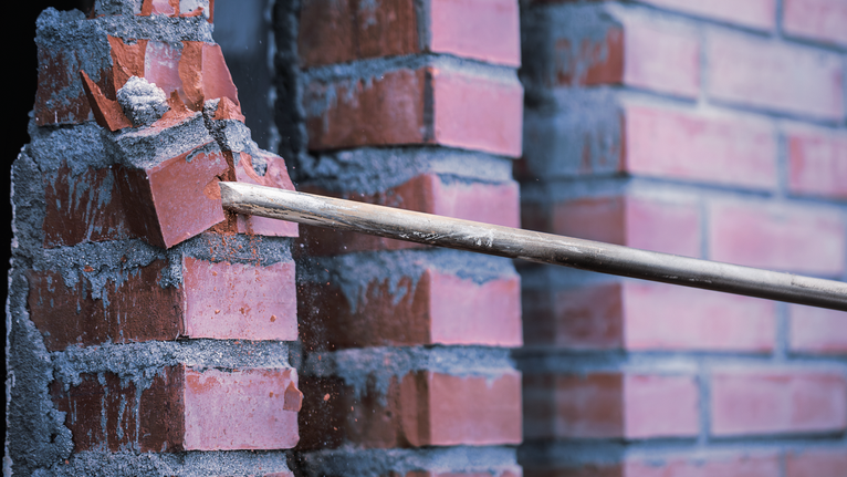 用鑿子將水泥牆上的紅磚鑿掉。
