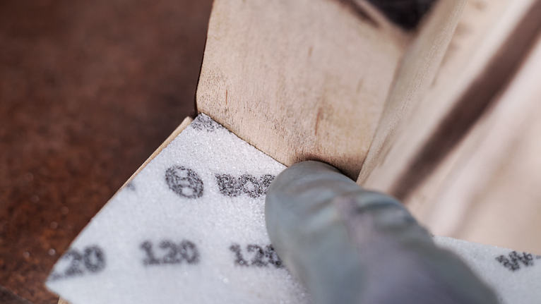 穿著安全設備的人正在打磨木質表面的角落。