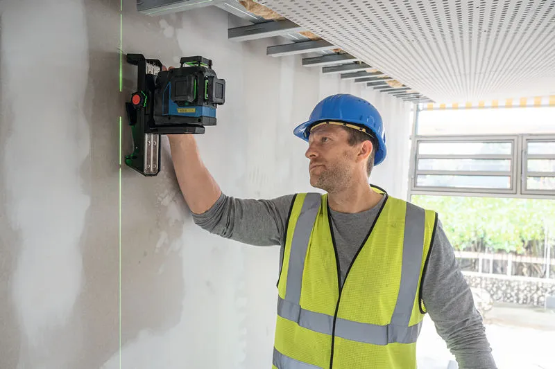 一名佩戴安全設備的人將雷射調平工具對準牆壁。.