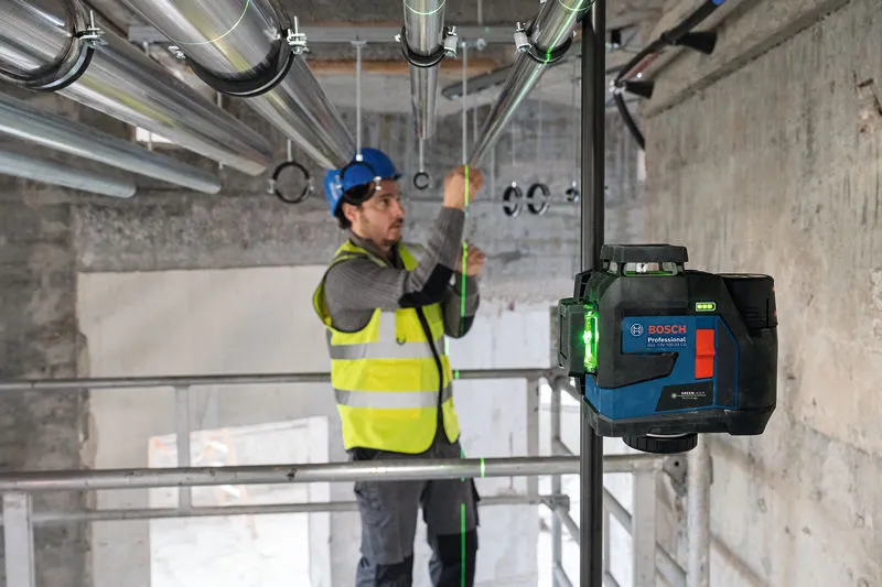 一名配戴安全設備的人員使用雷射調平工具對準管道。.