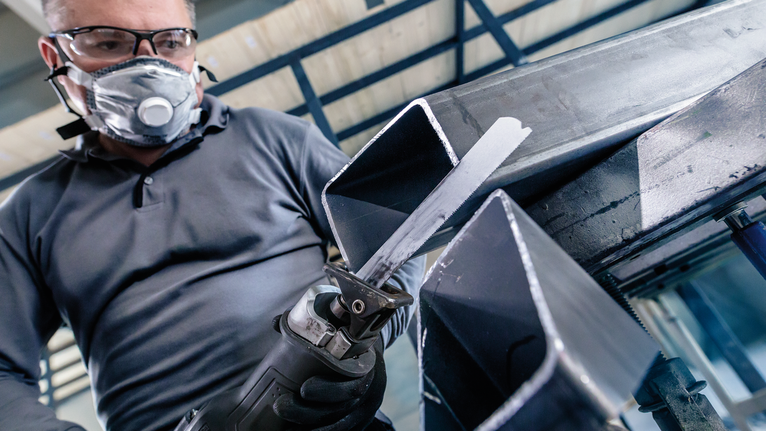 配戴安全設備的人員使用往復鋸切割金屬梁。