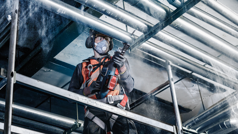 穿著安全設備的人員正在鑽入鷹架上的金屬管道。