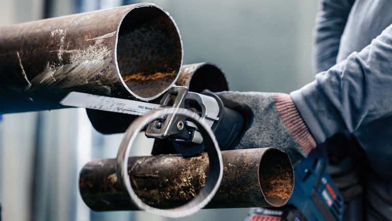 配戴安全設備的人用往復鋸切割一根生鏽的大金屬管。