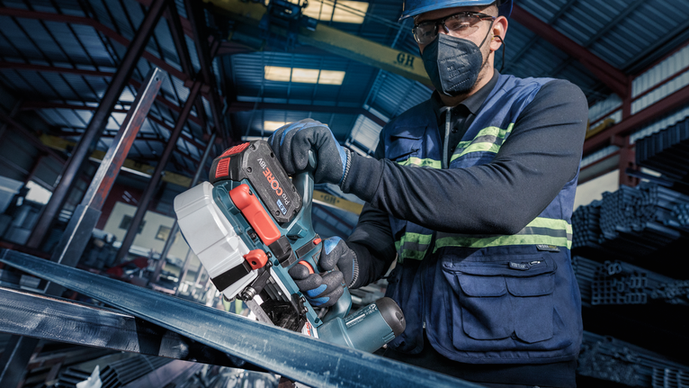 一名配戴安全設備的人員在工業環境中使用便攜式鋸子切割金屬。