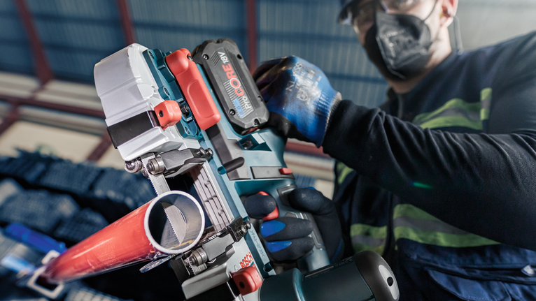 配戴安全設備的人員使用電動工具切割紅色管道。