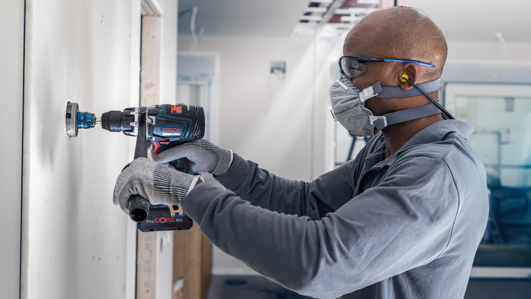 一名配戴安全設備的人員在牆上鑽孔。