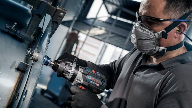 一名佩戴安全設備的人使用無線電動工具在金屬上鑽孔。