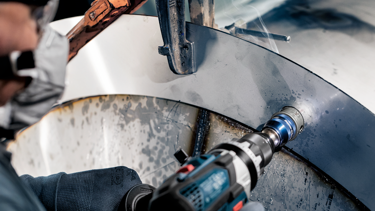 配戴安全設備的人員在彎曲的金屬表面上鑽孔。