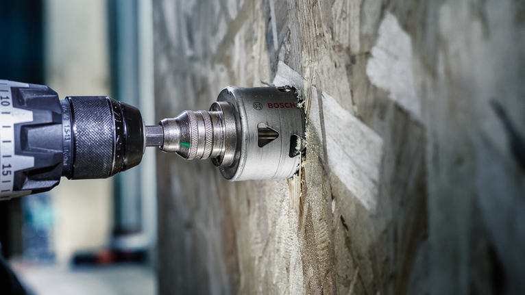 帶有孔鋸附件的電鑽正在切割木牆。