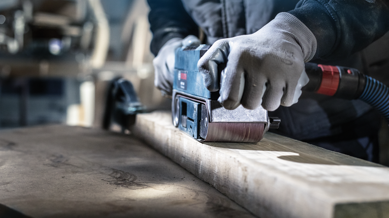 一名配戴安全設備的人員正在使用電動工具打磨木樑。
