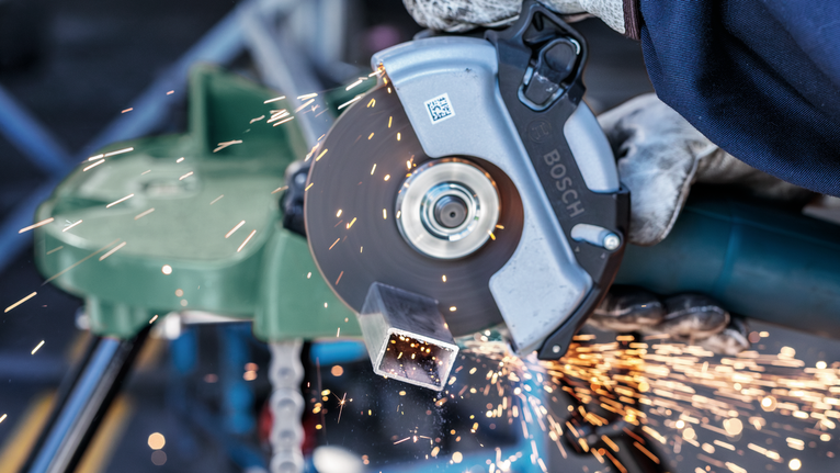 佩戴安全設備的人用角磨機切割金屬管，火花四濺。