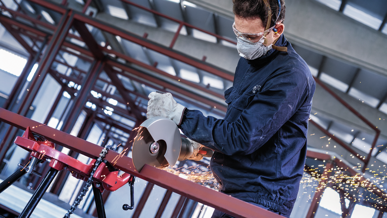 一名配戴安全設備的人使用電切割機切割金屬管道，產生火花。