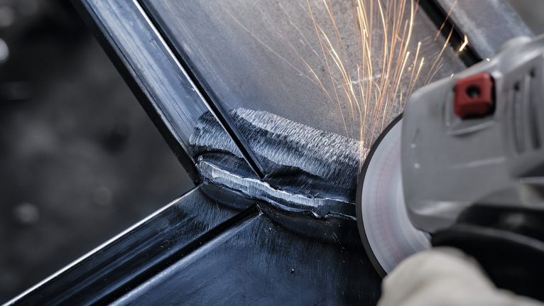 配戴安全設備的人研磨金屬焊縫，產生火花。.