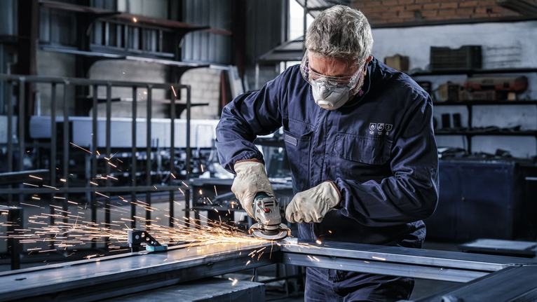 車間裡，穿著安全裝備的人員正在研磨金屬，產生火花。.