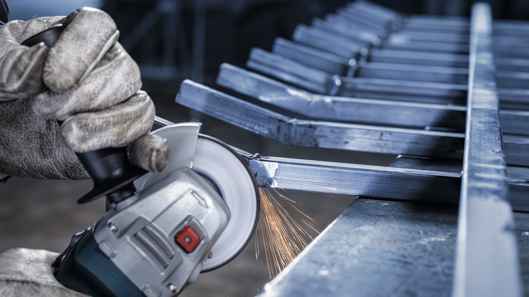 配戴安全設備的人員使用角磨機研磨金屬棒，產生火花。