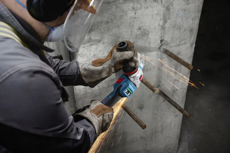 一名配戴安全設備的人員正在研磨混凝土牆上裸露的鋼筋。.
