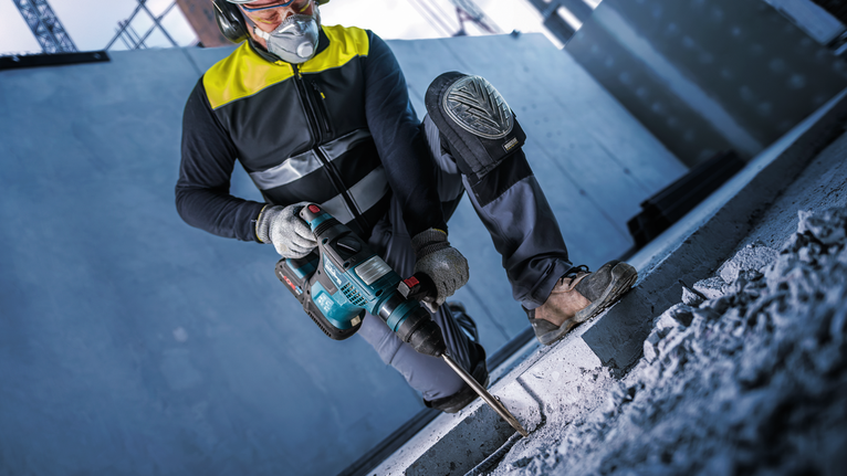 一名配戴安全設備的人員在建築工地上鑽混凝土。