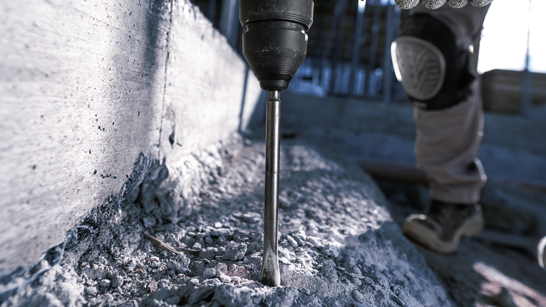 一名配戴安全設備的人員使用旋轉錘在混凝土中鑽孔。