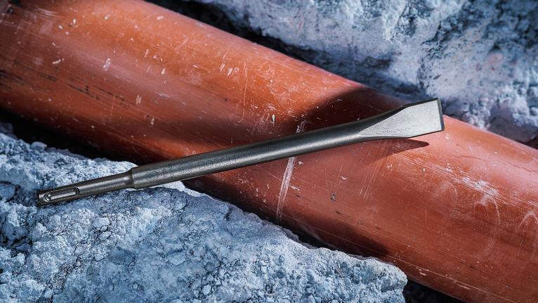 一把鑿子放在一根被破碎的混凝土包圍的管道上。