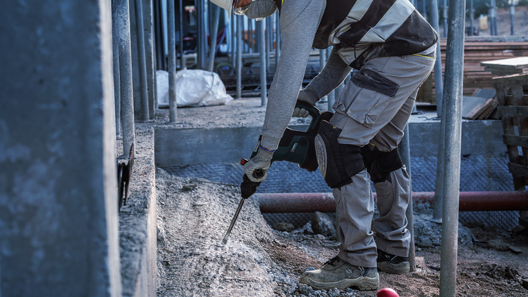 在建築工地上，一名配戴安全設備的人員使用電動工具來破碎混凝土。