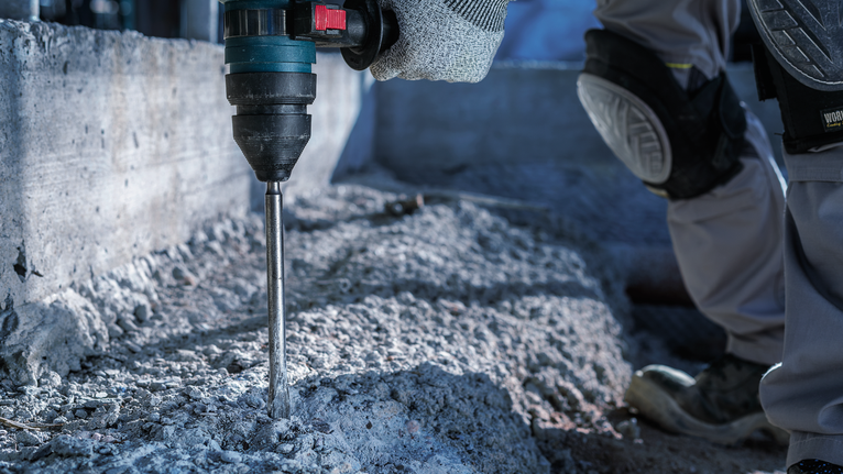 一名配戴安全設備的人員在建築工地上鑽混凝土。