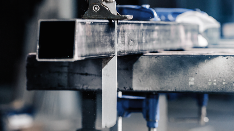 金屬鋸在工作台上切割鋼製矩形管。