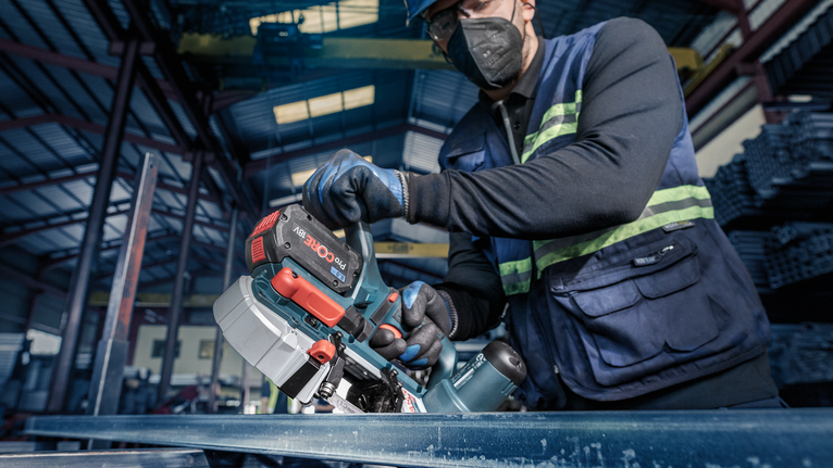 一名佩戴安全裝備的人使用無線帶鋸切割金屬梁。