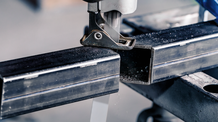 拼圖鋸在工作台上切割金屬矩形管。