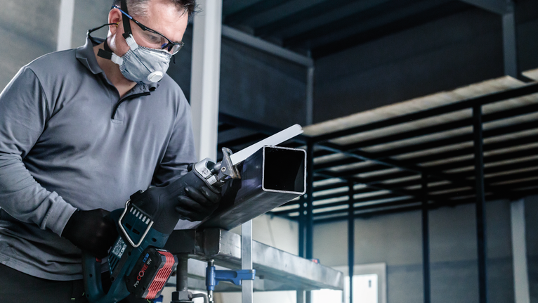 一名配戴安全設備的人員使用往復鋸切割金屬管路。