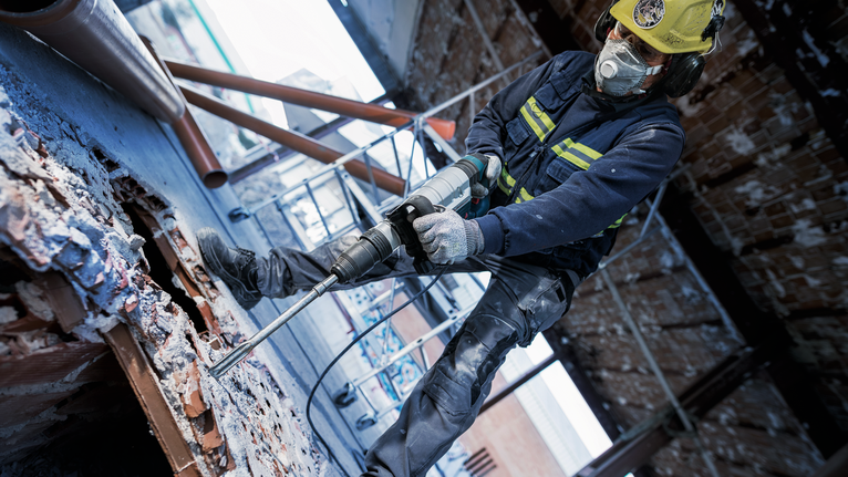 一名身著安全設備的人員在拆除現場鑽入混凝土。