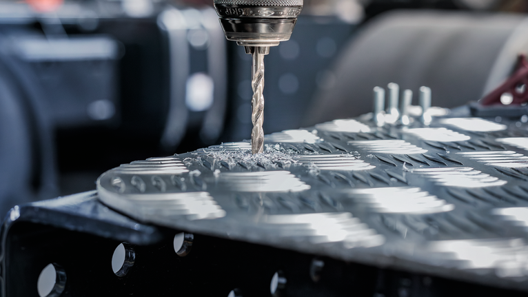 鑽頭在有紋理的金屬板上鑽孔，產生金屬屑。