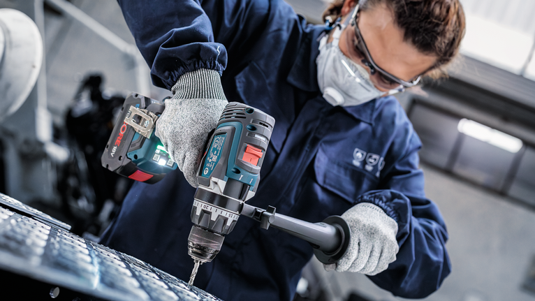 配戴安全設備的人員使用無線電動工具鑽入金屬。