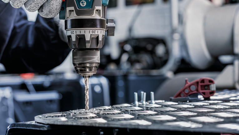 配戴安全設備的人員在金屬板上鑽孔。