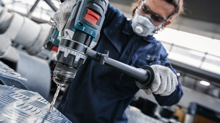 配戴安全設備的人員使用電動工具鑽入紋理金屬。