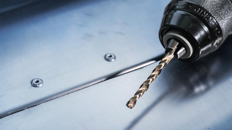 帶有金屬鑽頭的電鑽放在鋼板上。