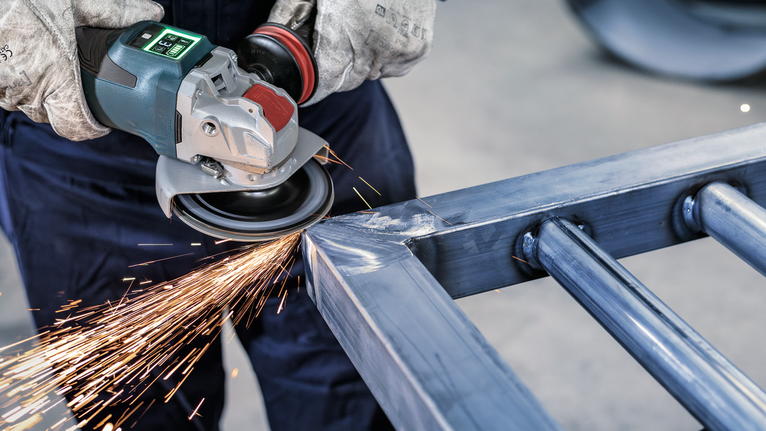 一名配戴安全設備的人員正在用角磨機打磨金屬框架。