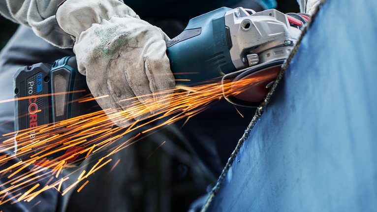 一名配戴安全設備的人研磨金屬，產生一陣火花。