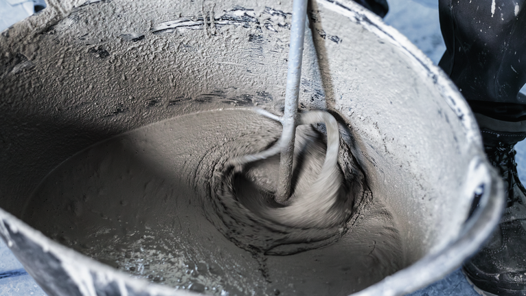 一名配戴安全設備的人員使用電動工具在桶中攪拌水泥。