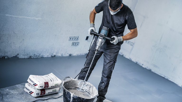 配戴安全設備的人員使用動力攪拌機攪拌桶中的水泥。