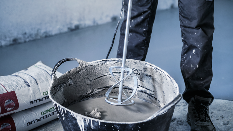 配戴安全設備的人員使用電動工具在大桶中攪拌水泥。