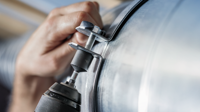 一個人用電動工具將螺栓擰緊到大型金屬管道上。