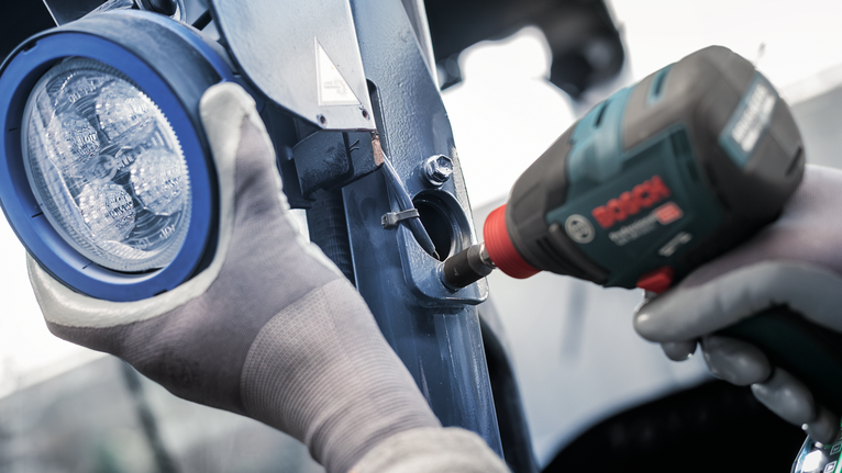 配戴安全設備的人員使用電動工具將燈安裝在金屬上。