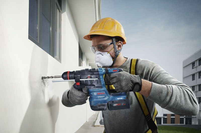 一名配戴安全設備的人員使用電動工具在外牆上鑽孔。.