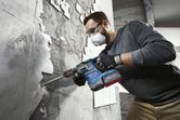 一名佩戴安全設備的人員使用旋轉錘將瓷磚從牆上拆除。.