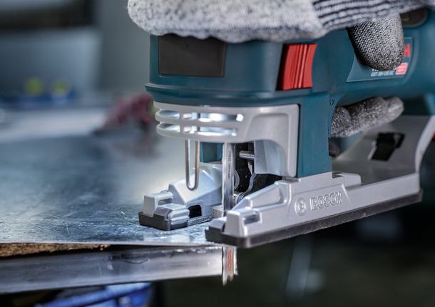 配戴安全設備的人員使用曲線鋸切割金屬板。