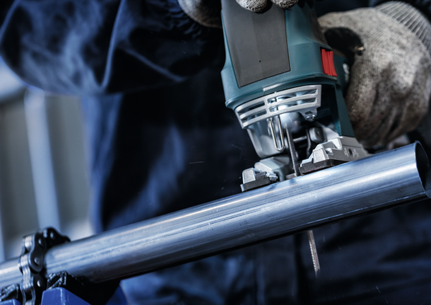 配戴安全設備的人員使用曲線鋸切割金屬管。