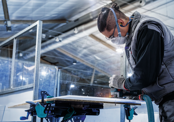 配戴安全設備的人員使用電動工具切割木板。